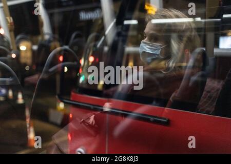 Ragazza bionda che indossa la maschera facciale riflessa nella finestra degli autobus di notte, Londra, 21 febbraio 2021 Foto Stock