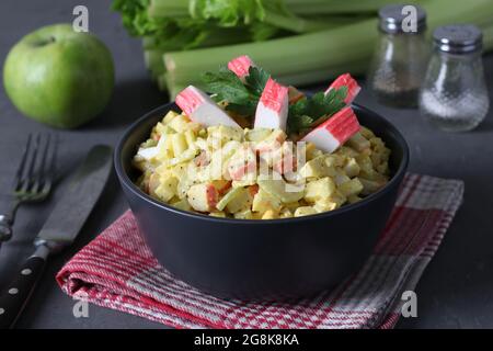 Insalata con bastoncini di granchio, sedano, mele e uova di quaglia in un recipiente scuro su sfondo grigio. Mangiare sano. Foto Stock