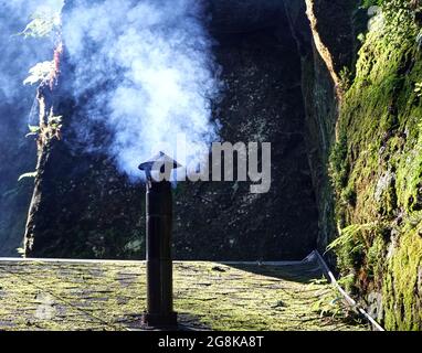 Fumo che sale da un sottile camino arrugginito sul tetto di ciottoli di una capanna in Svizzera sassone Foto Stock