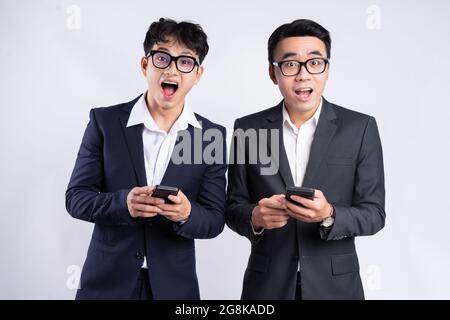 Giovani dipendenti vietnamiti maschi in tute con espressioni facciali stupite che tengono telefoni cellulari Foto Stock