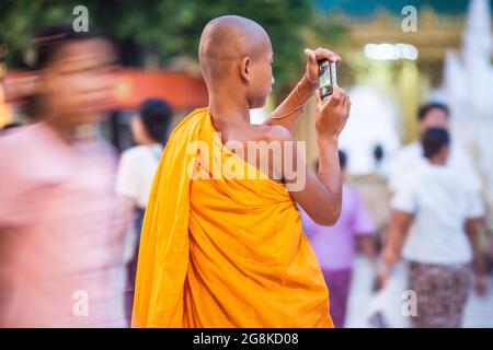 Il giovane monaco birmano che indossa abiti arancioni scatta foto con la fotocamera, Shwedagon Pagoda, Yangon, Myanmar Foto Stock