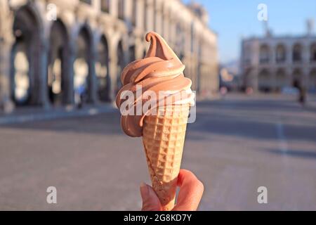 Delizioso gelato al cioccolato e alla vaniglia Soft servire in mano contro gli edifici vintage sfocati Foto Stock