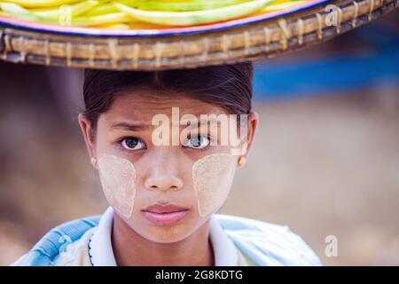 Giovane grazioso venditore di frutta birmano con vassoio di frutta sulla testa e thanaka sul viso guarda in su alla finestra degli autobus, Magwe, Myanmar Foto Stock