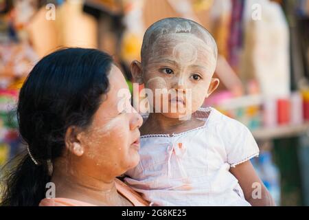 Giovane ragazza birmana con testa rasata e viso pieno di motivi thanaka di pasta gialla trucco cosmetico portato da sua madre, Monte Pope, Myanmar Foto Stock