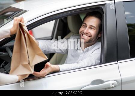 Il corriere di consegna del cibo dà i sacchetti di carta all'uomo in automobile. Alimenti di sicurezza consegnati Foto Stock