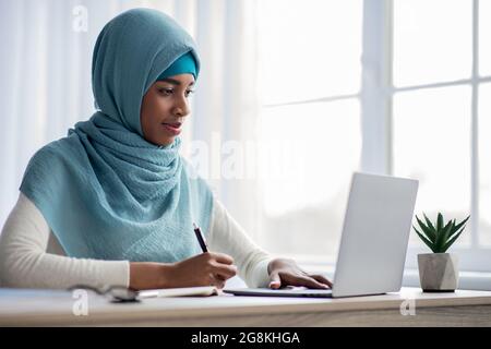 Concetto di apprendimento online. Black Muslim Lady a Hijab usando il laptop a casa Foto Stock