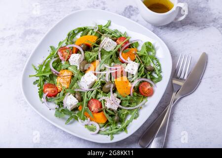 Insalata calda con zucca, formaggio feta, pomodori, capperi, rucola e cipolla rossa. Primo piano. Foto Stock