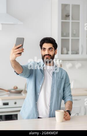 Blogger arabo che fa streaming di video o foto per i social media. Giovane uomo che tiene smartphone, prendendo selfie, raccolto Foto Stock
