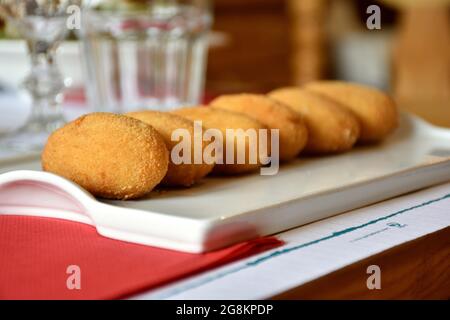 Servire di sei crocchette su un piatto bianco. Posizionato in una fila e messo a fuoco sul primo. Piatto da ristorante, tipico della Spagna. Foto Stock