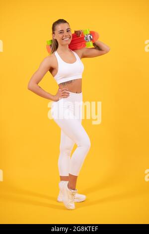 Happy fit ragazza skater tenere pennyboard sfondo giallo, penny bordo Foto Stock