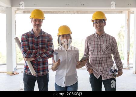 Diversity team di ingegneri, una donna e due uomini, in piedi insieme e sorridendo alla macchina fotografica durante il lavoro in cantiere. Foto Stock