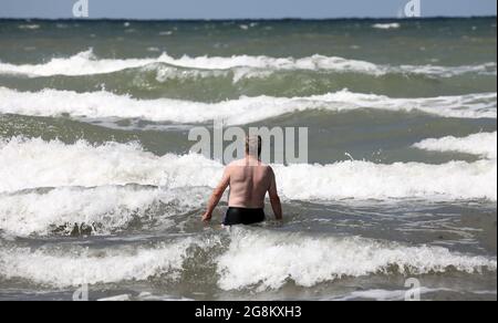 19 luglio 2021, Meclemburgo-Pomerania occidentale, Warnemünde: Un uomo cammina nel Mar Baltico, che è scagliato dal forte vento. Foto: Bernd Wüstneck/dpa-Zentralbild/ZB Foto Stock