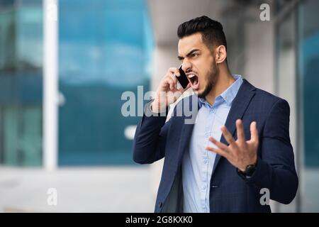 Furioso uomo arabo nel vestito che ha conversazione telefonica Foto Stock