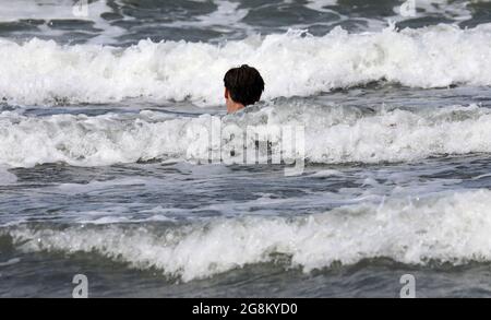 19 luglio 2021, Meclemburgo-Pomerania occidentale, Warnemünde: Un giovane cammina nel Mar Baltico, che è scagliato dal forte vento. Foto: Bernd Wüstneck/dpa-Zentralbild/ZB Foto Stock