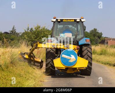 Uomo in un trattore che rasa erba verga in una corsia di campagna in estate. Molto Hadham, Hertfordshire Luglio 2021 Foto Stock