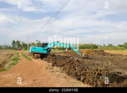 Il moderno escavatore sta lavorando su lavori di terra per scavare gli stagni vicino al campo di risaie, immagazzinando l'acqua per l'uso in agricoltura in estate, davanti Foto Stock