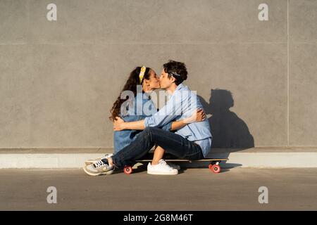 Coppia giovane amorevole seduta su tavola lunga baciando. Felice uomo e donna in amore abbracciando l'esterno Foto Stock