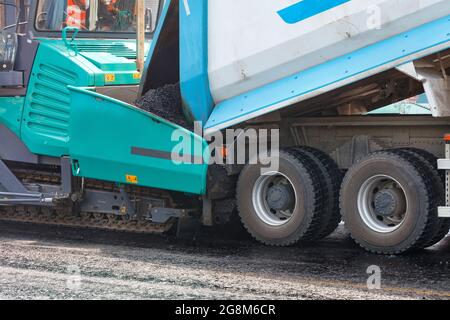 Un dumper scarica l'asfalto dal suo cassone in un'asfaltatrice in un cantiere. Primo piano, spazio per la copia. Foto Stock