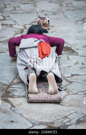 Pellegrina femminile giacente sul pavimento dopo essersi prostrata. Facendo il 'Barkhor Kora', un circuito devozionale di pellegrinaggio intorno al vecchio Tempio di Jokhang Foto Stock