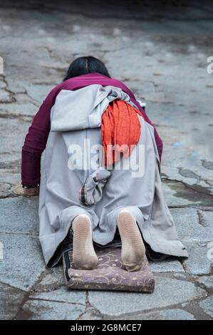 Pellegrina femminile giacente sul pavimento dopo essersi prostrata. Facendo il 'Barkhor Kora', un circuito devozionale di pellegrinaggio intorno al vecchio Tempio di Jokhang Foto Stock