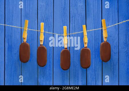 c'è un sacco di gelati al cioccolato appesi sulla corda vicino a sfondo blu. dessert estivo caldo e un delizioso concetto di cibo Foto Stock