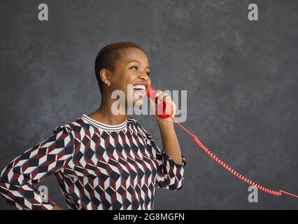 Felice giovane donna nera che tiene il ricevitore del suo telefono fisso e parla Foto Stock