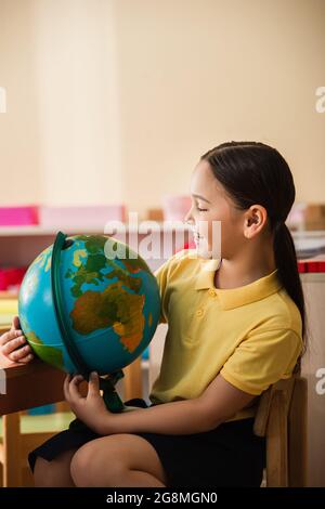 felice ragazza asiatica guardando il mondo a montessori scuola Foto Stock