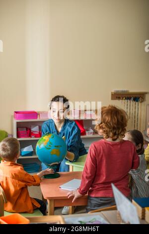 insegnante sorridente che parla con i bambini vicino a tutto il mondo in classe Foto Stock