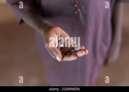 Ciò è un'immagine di un bambino africano che tiene un supplemento o una pillola medica nella sua mano per mostrare il trattamento di una carenza o di una malattia. Foto Stock