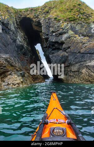 Kayak in mare attraverso una grotta marina sulla costa di Pembrokeshire Foto Stock