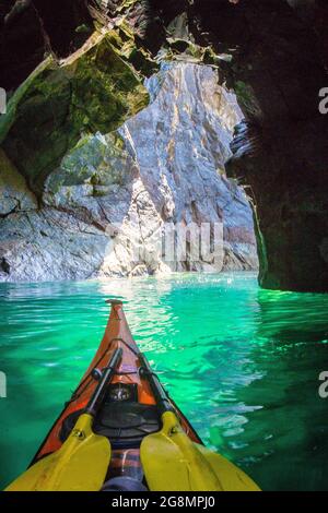 Kayak in mare attraverso una grotta marina sulla costa di Pembrokeshire Foto Stock