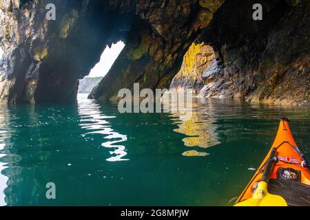 Kayak in mare attraverso una grotta marina sulla costa di Pembrokeshire Foto Stock