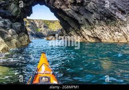 Kayak in mare attraverso una grotta marina sulla costa di Pembrokeshire Foto Stock