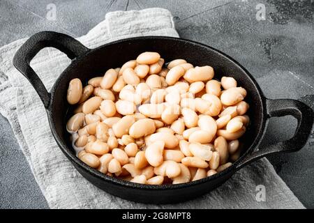 Set di fagioli bianchi in scatola, in padella di ghisa, su fondo grigio in pietra Foto Stock