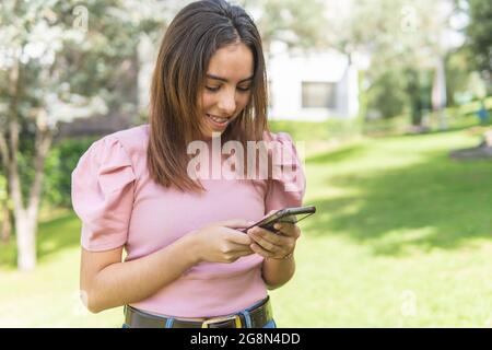 Ragazza teenage latina con parentesi graffe che guarda sorridentemente il suo telefono cellulare in un parco Foto Stock