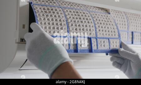 Persona che rimuove il filtro del condizionatore d'aria, mano del tecnico uomo che lavora tirando il filtro polveroso dal condizionatore d'aria alla pulizia nella stanza a casa Foto Stock