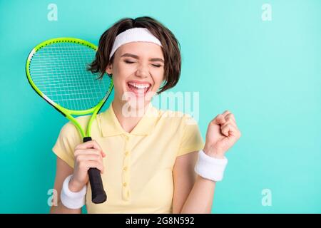 Ritratto di attraente sportivo allegra ragazza sognante che tiene in mano racchetta celebrando vittoria isolato su luminoso sfondo turchese teal colore Foto Stock