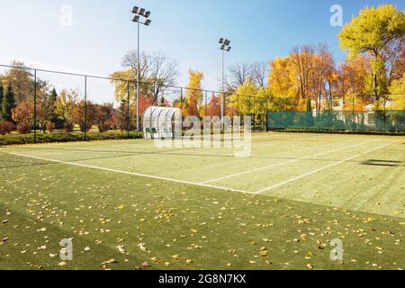 Campo da tennis nel parco autunnale. Il parco giochi è coperto di foglie caduti. Foto Stock