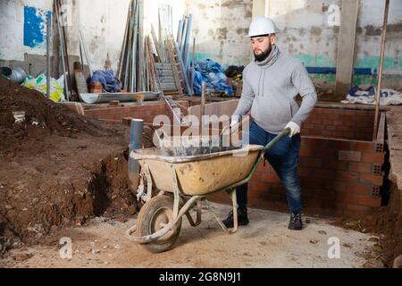 Operatore che porta secchio con Malta di cemento su carrello Foto Stock