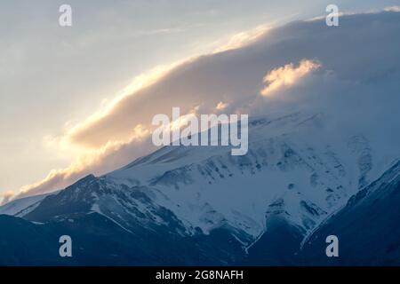 Tramonto dietro la pendenza del Monte Damavand, il più alto stratovulcano in Asia. Pomeriggio parzialmente nuvoloso nelle montagne dell'Iran. Le nuvole CAP si riuniscono Foto Stock