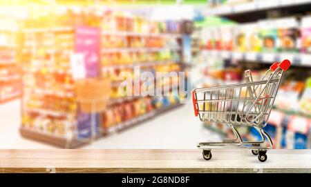 Supermercato alimentari tavolo sfondo con carrello. Cibo e generi alimentari sfocati sugli scaffali del negozio. Foto di alta qualità Foto Stock