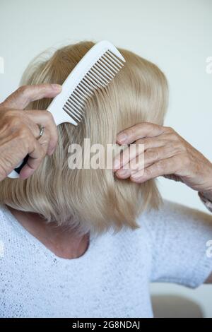 Una donna anziana che combatte i suoi capelli. Primo piano. Routine quotidiana degli anziani. Foto Stock
