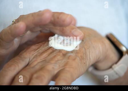 Le donne anziane applicano la crema della mano sulle sue mani. Primo piano. Routine quotidiana degli anziani. Foto Stock