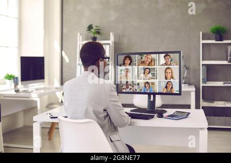Donna nera che ha riunione di affari in linea con il gruppo della gente sul calcolatore d'ufficio Foto Stock