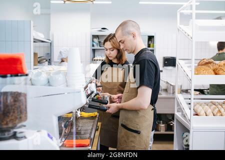 Due fornai, giovane uomo e donna che lavorano in cucina, desiderosi del loro compito. Vista laterale. Foto Stock