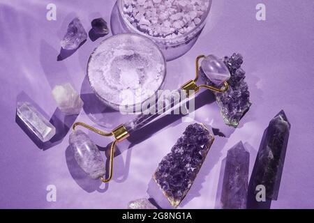 Amethyst cristalli Gha sha rullo di massaggio raschietto e prodotto di bellezza. Attrezzi idratanti e per la cura della pelle. Concetto di benessere. Foto Stock