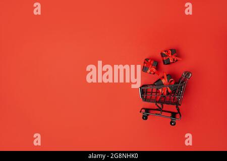 scatole regalo nere con arco rosso nel carrello, vendita del venerdì nero. sfondo rosso, spazio copia Foto Stock