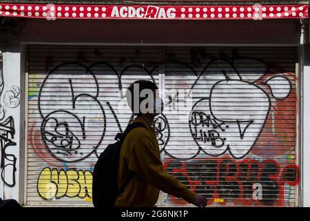 Un giovane giapponese, indossando una maschera contro COVID19, cammina di fronte a un negozio chiuso Takeshita Dori, coperto di graffiti Harajuku, Tokyo, Giappone Foto Stock