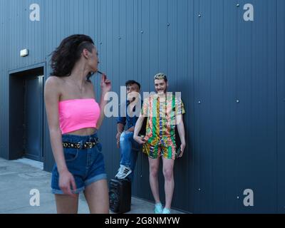 Due maschi in piedi al muro con un altoparlante e guardando una femmina che passa Foto Stock