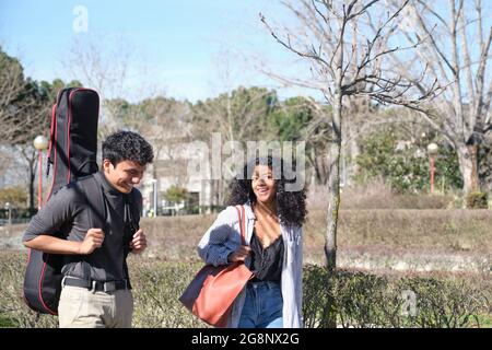 Amici latini che camminano per il campus universitario con una custodia per chitarra. Vita universitaria. Foto Stock